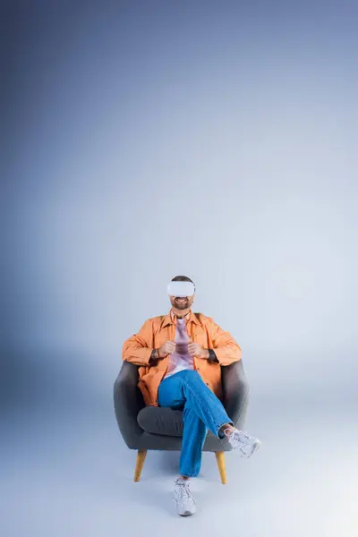 Um homem em um fone de ouvido VR confortavelmente relaxando em uma cadeira com os pés para cima em um estúdio. — Fotografia de Stock