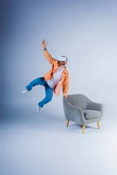 A person wearing a VR headset jumps energetically next to a chair in a studio setting. — Stock Photo