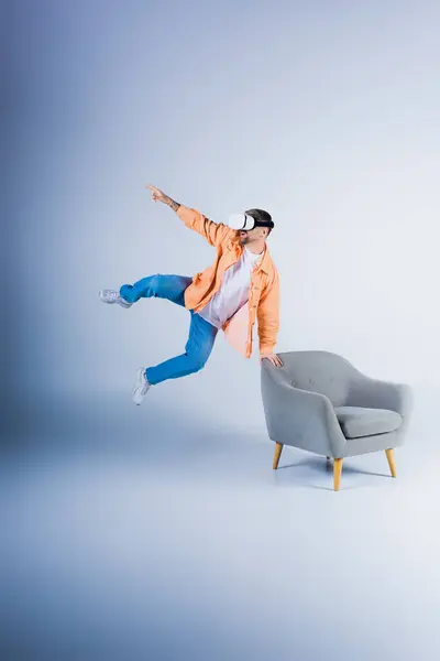 Um homem usando um fone de ouvido VR salta energicamente em um estúdio, voando sobre uma cadeira com agilidade e graça. — Fotografia de Stock
