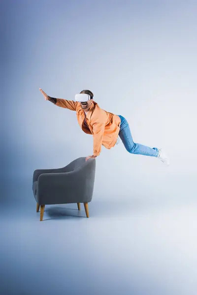 A man in a VR headset performs a gravity-defying trick on a chair in a futuristic studio setting. — Stock Photo