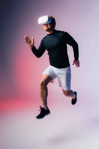 Un hombre con camisa negra y pantalones cortos blancos salta alegremente en el aire, creando sombras dramáticas en un ambiente de estudio. - foto de stock