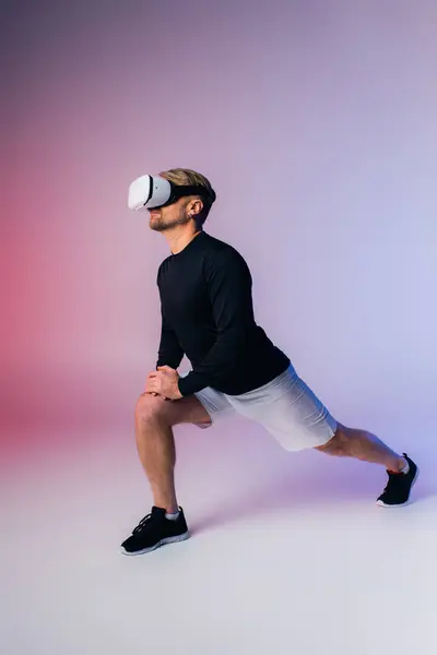 Um homem de camisa preta e calções brancos realiza um agachamento em um estúdio, imerso em uma experiência de realidade virtual. — Fotografia de Stock