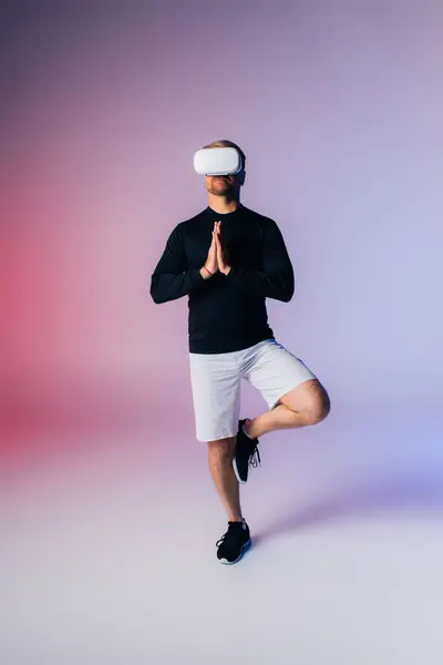 Un hombre con una camisa negra y pantalones cortos blancos golpea elegantemente una pose de yoga en un ambiente de estudio. - foto de stock