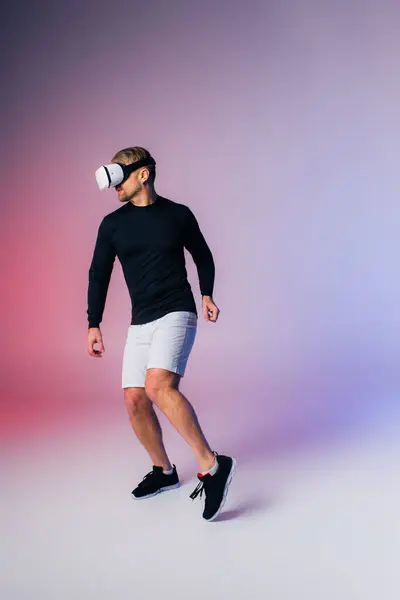 A man in a black shirt and white shorts showcases his moves in a virtual reality headset in a studio setting. — Stock Photo