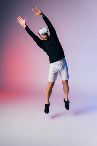 Um homem usando um fone de ouvido VR está pulando no ar enquanto segura uma raquete de tênis virtual em um estúdio. — Fotografia de Stock