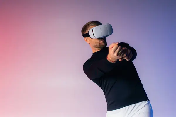 Un hombre con un casco VR balancea un bate de béisbol con los ojos vendados en un entorno de estudio, mostrando entrenamiento deportivo de realidad virtual. - foto de stock