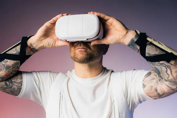 Un hombre con una camisa blanca sostiene un objeto blanco sobre su cabeza, inmerso en un auricular de realidad virtual en un entorno de estudio. - foto de stock