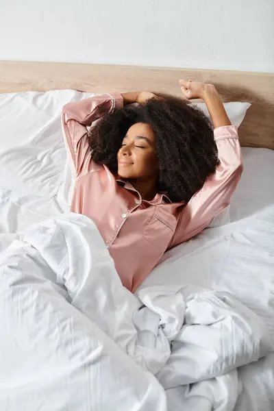 Curly African American woman in pajamas peacefully laying on a bed with white sheets in the morning. — Stock Photo