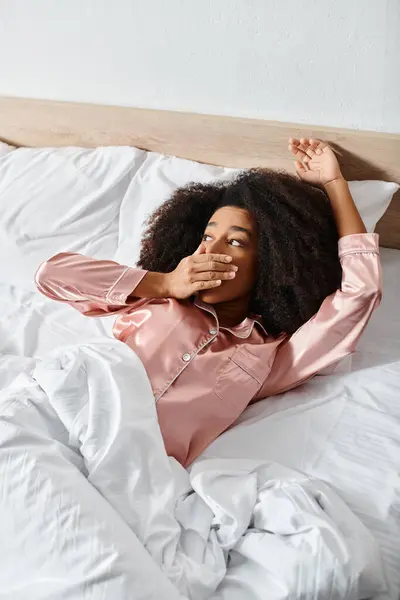 Uma mulher afro-americana encaracolada de pijama está pacificamente deitada em uma cama coberta de lençóis brancos em um ambiente sereno da manhã.. — Fotografia de Stock