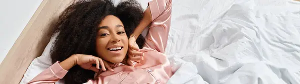 Curly African American woman in pajamas lying on bed, hair floating in the air with a dreamy and serene atmosphere. — Stock Photo