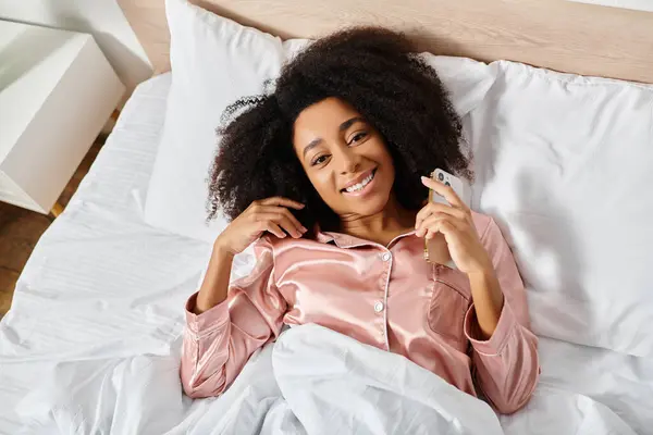 Lockige Afroamerikanerin im Schlafanzug auf dem Bett liegend, ein Papier mit nachdenklichem Gesichtsausdruck in der Hand. — Stockfoto