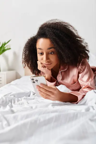 Riccio donna afroamericana in pigiama sdraiato sul letto, assorto in tablet al mattino. — Foto stock