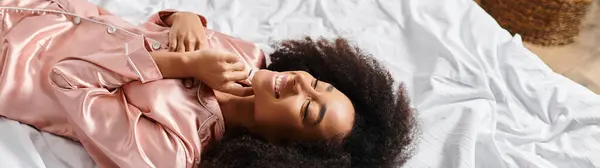 Curly mulher afro-americana de pijama deitado na cama em uma cena de manhã aconchegante. — Fotografia de Stock