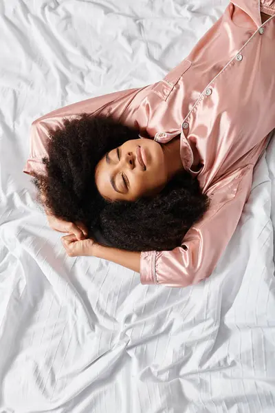 A curly African American woman in pajamas peacefully lays on a white bed in a bedroom. It is morning time. — Stock Photo