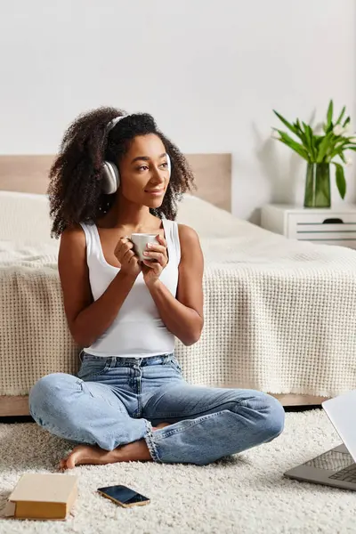 A curly African American woman in a tank top sits on the floor, deeply engrossed in listening to music. — Stock Photo