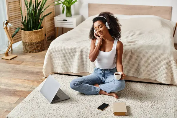 Curly African American woman in a tank top sitting on the floor, engaged in a phone conversation in a modern bedroom. — Stock Photo