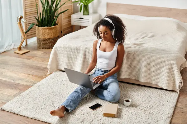 A woman with curly hair sits on the floor using a laptop in a modern bedroom. — Stock Photo