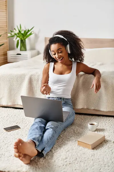Кучерява афроамериканка, сидячи на підлозі в сучасній спальні, захоплена використанням ноутбука. — стокове фото