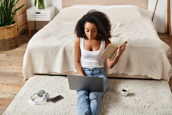 Curly African American woman in tank top sitting on floor, focused on her laptop in a modern bedroom. — Stock Photo