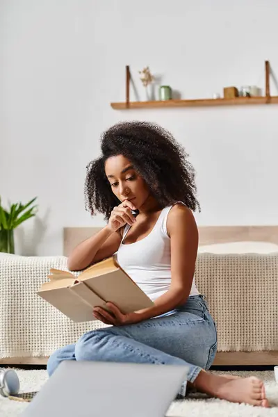 Lockige Afroamerikanerin im Tank-Top sitzt in ein Buch vertieft auf dem Boden und findet in ihrem ruhigen Moment Frieden. — Stockfoto