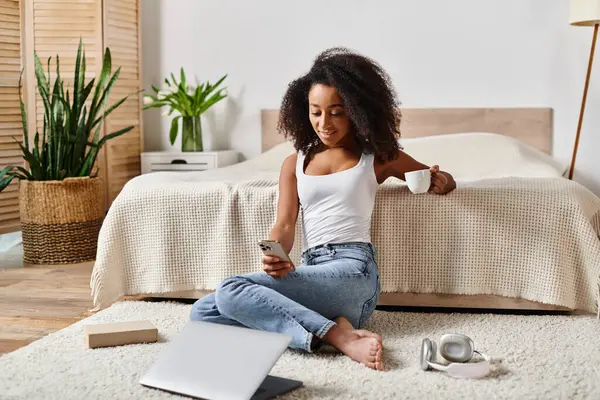 Lockige Afroamerikanerin sitzt auf dem Boden neben Laptop im modernen Schlafzimmer. — Stockfoto