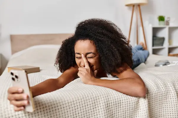 A curly African American woman in a tank top peacefully rests with closed eyes on a modern bed in a bedroom. — Stock Photo