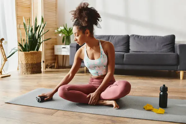 Curly African American woman in activewear sitting on a yoga mat in a cozy living room, practicing mindfulness. — Stock Photo