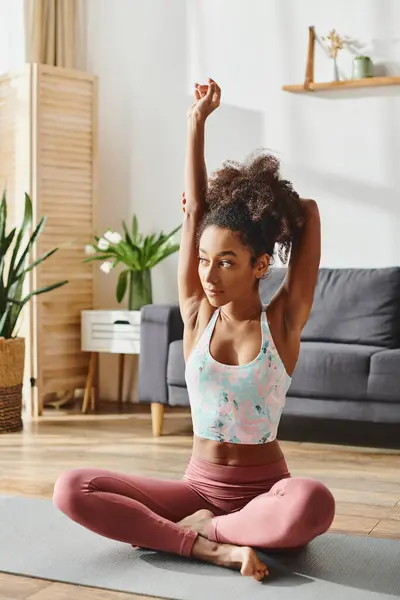 Eine lockige Afroamerikanerin in aktiver Kleidung praktiziert Yoga in ihrem ruhigen Wohnzimmer und findet Frieden und Balance. — Stockfoto