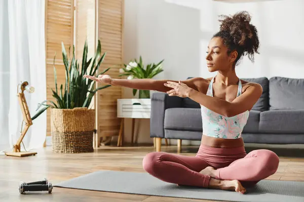 A curly African American woman in activewear practices yoga in a serene living room setting. — Stock Photo
