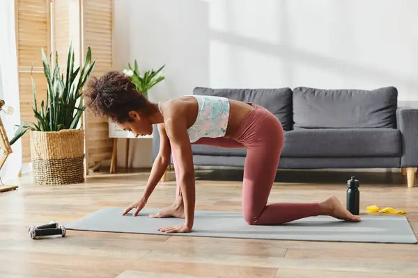A curly African American woman in activewear gracefully balances on a yoga mat in a challenging yoga pose. — Stock Photo