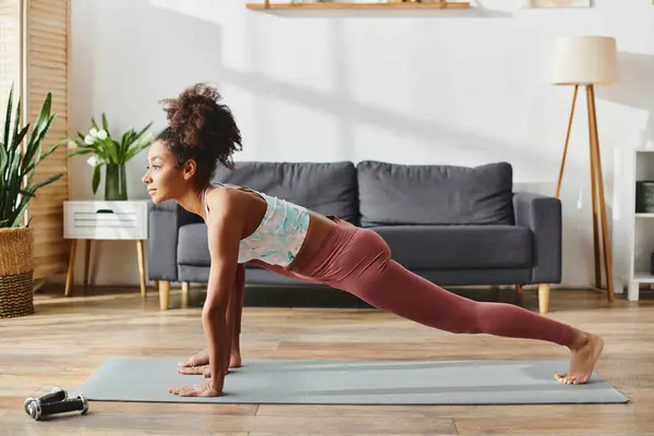 Curly African American woman in active wear performing a yoga pose in a cozy living room. — Stock Photo