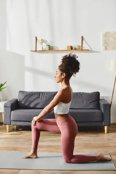 Curly African American woman in activewear gracefully performing a yoga pose in a cozy living room. — Stock Photo