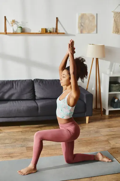 Une femme afro-américaine aux cheveux bouclés pratique une pose de yoga dans un cadre confortable de salon. — Photo de stock