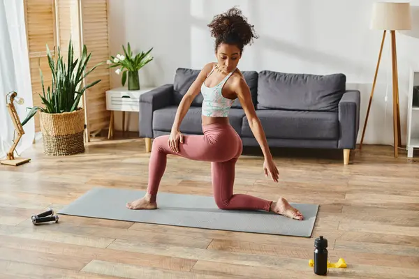 Une afro-américaine frisée en tenue active exécute gracieusement une posture de yoga dans son salon. — Photo de stock