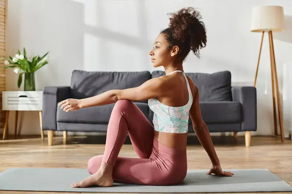 Curly African American woman in activewear gracefully executes a yoga pose on a mat at home. — Stock Photo