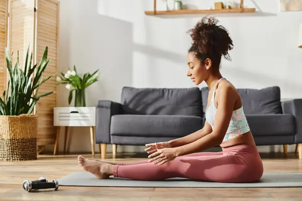 Curly African American woman in active wear practices yoga on a mat in a cozy living room. — Stock Photo