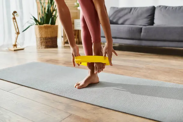 Cropped African American woman on yoga mat holding yellow elastics in home workout session. — Stock Photo