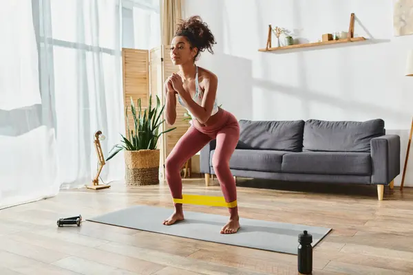 A curly African American woman in activewear practices with elastics in a cozy living room setting. — Stock Photo