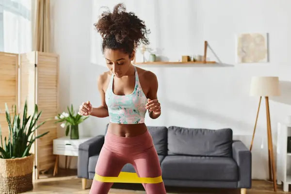 Mulher afro-americana encaracolado em esportes sutiã e leggings exercícios em casa, mostrando força e dedicação. — Fotografia de Stock