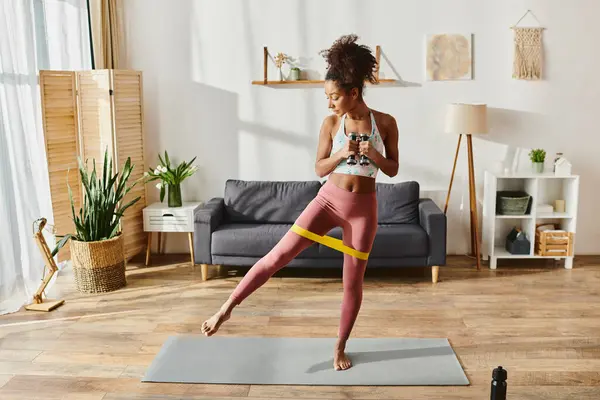 Femme afro-américaine en tenue active pratiquant le yoga dans un cadre confortable salon. — Photo de stock