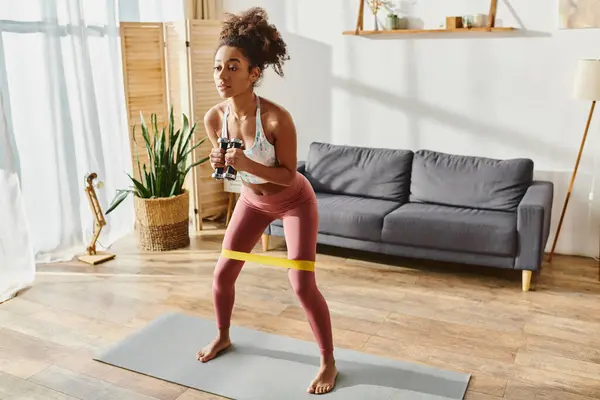 Curly mulher afro-americana em activewear graciosamente golpeia uma pose de ioga em um tapete em casa. — Fotografia de Stock