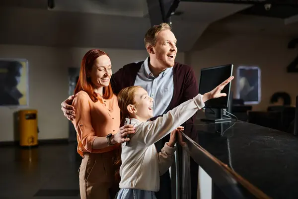 A happy family, a man, woman, and child, are captivated by something on the cinema wall, engrossed in the moment. — Stock Photo