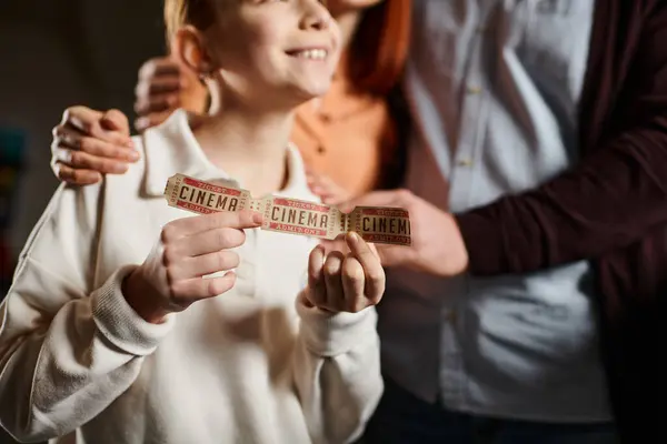 Kid joyfully hold up a colorful tape, symbolizing unity and bond with family during a cinema outing. — Stock Photo