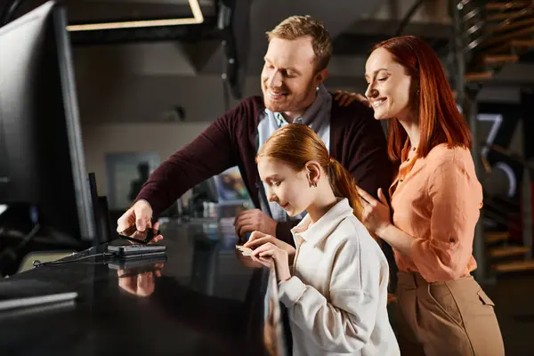 Tres personas, una familia feliz, se reunieron alrededor de una pantalla de computadora, absortos en lo que ven. - foto de stock
