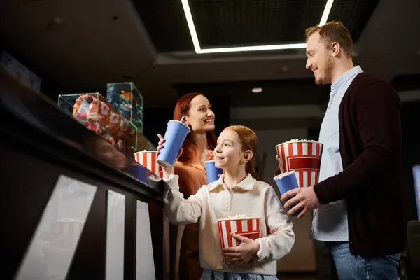 A happy family standing in a circle, holding cups and chatting joyfully in a cinema setting. — Stock Photo