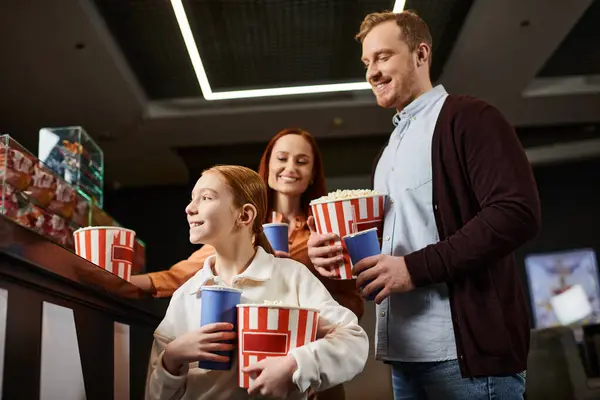 A happy family stands in a circle, holding cups, enjoying each others company in a cinema. — Stock Photo