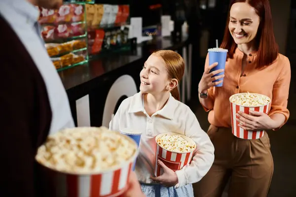 Живая группа людей, стоящих возле бара, наслаждающихся попкорном и оживленными разговорами в кинотеатре. — стоковое фото