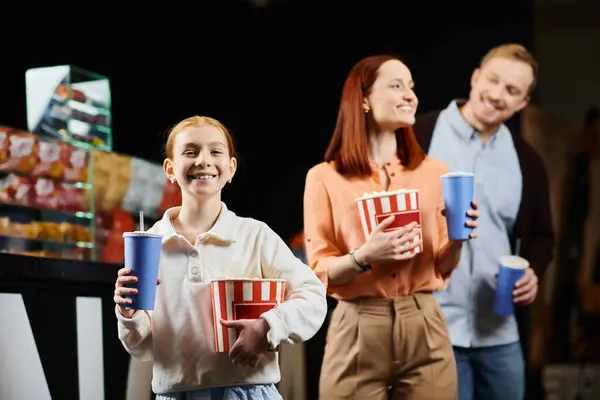 Une famille heureuse profitant d'un moment de collage au cinéma, debout ensemble et tenant des tasses. — Photo de stock