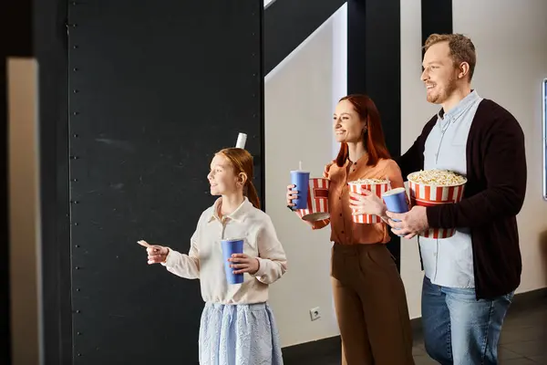 A happy family stands close, holding popcorn in a cinema setting, enjoying a cheerful moment together. — Stock Photo