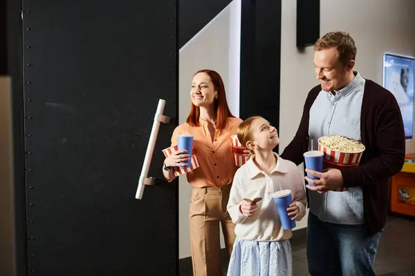 Un hombre, una mujer y un niño felices sosteniendo copas de palomitas de maíz, disfrutando de un tiempo de calidad juntos en el cine. - foto de stock